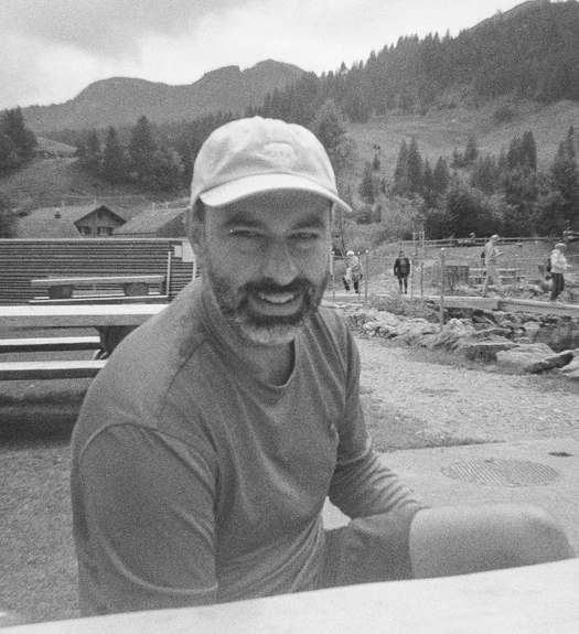 Jovan in a cap, smiling, at a mountain lake (black and white), taped to the iMac