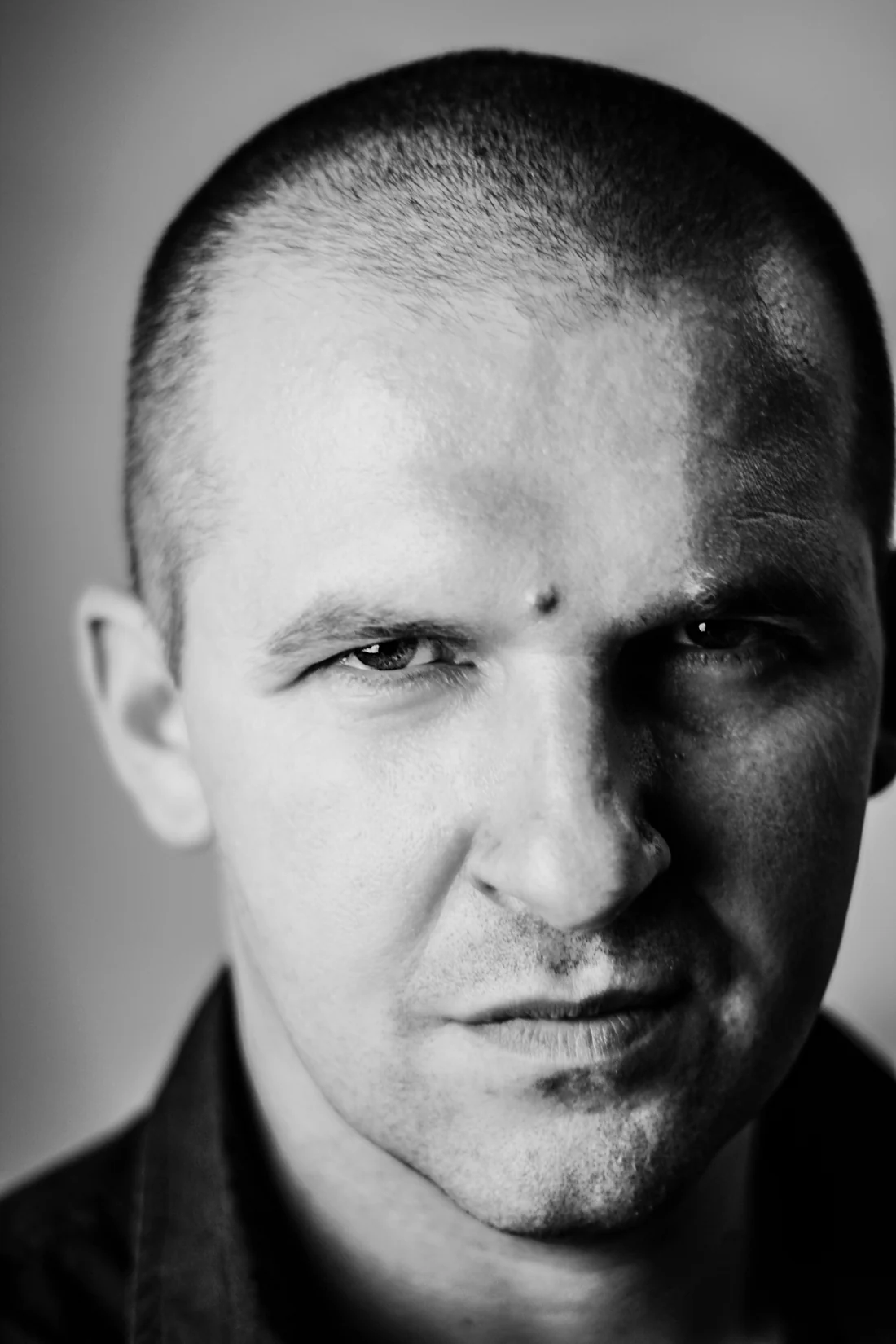 Black-and-white portrait of a man with a shaved head, looking straight at the camera