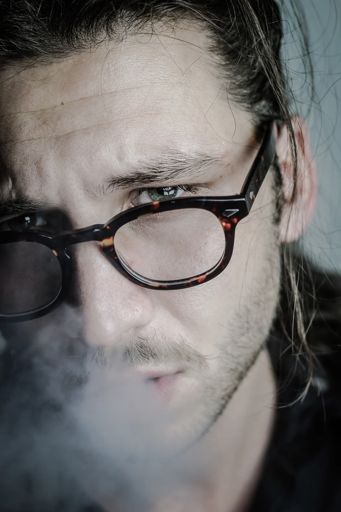 Portrait of a man in glasses breathing out smoke