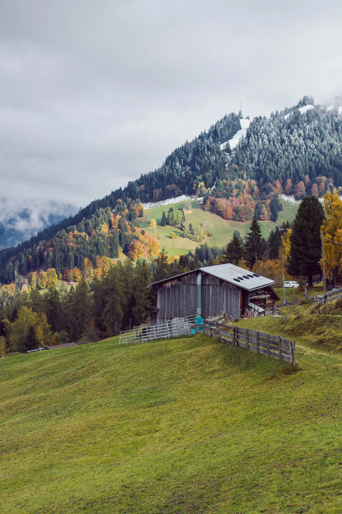A wooden cabin on a green slope below an autumn mountain in Graubünden