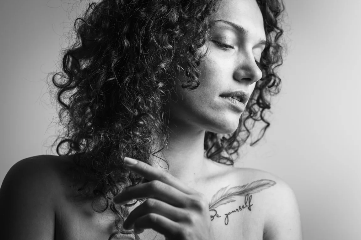 Black-and-white portrait of a woman with curly hair and a tattoo on her collarbone