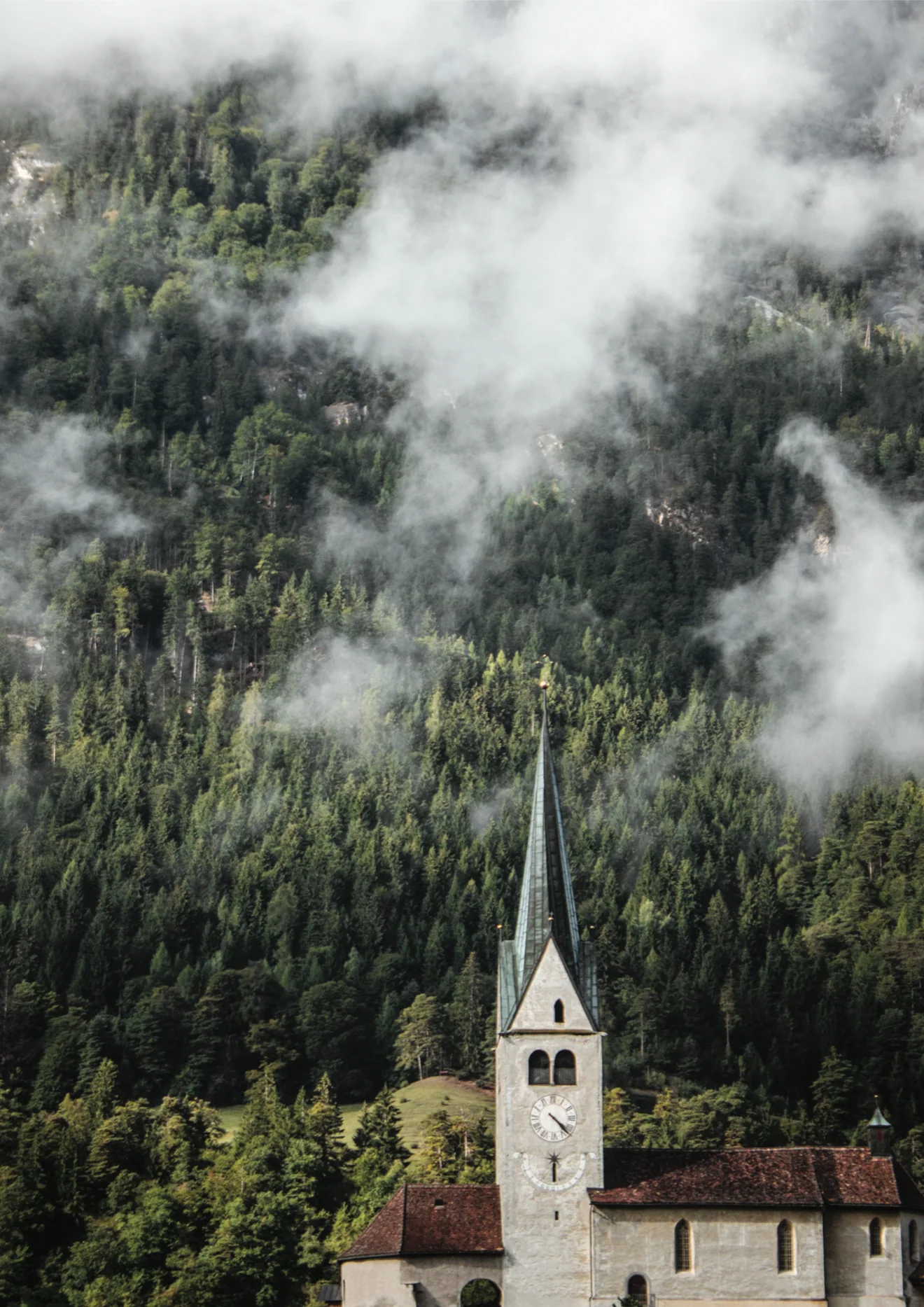 A church below forested mountains in low cloud